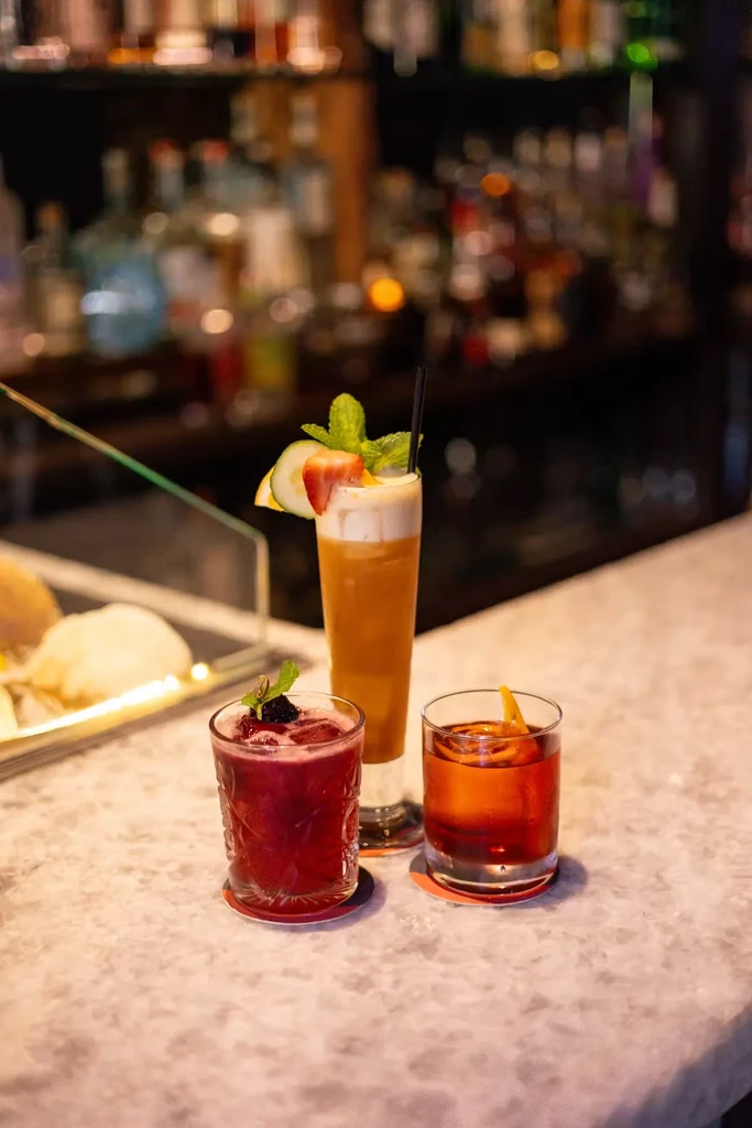 Three colorful cocktails with garnishes on a marble bar counter.
