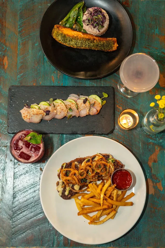 A table of entrees: salmon, ceviche, steak with fries, and cocktails.