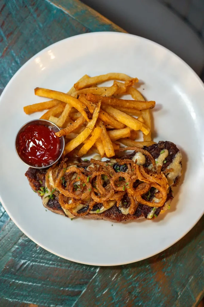 Steak with fried onions, french fries, and ketchup on a white plate.