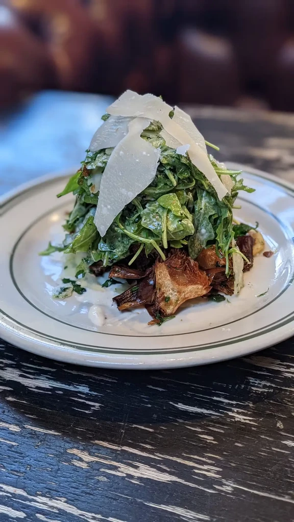 Arugula salad with shaved cheese, roasted artichokes, and white sauce.