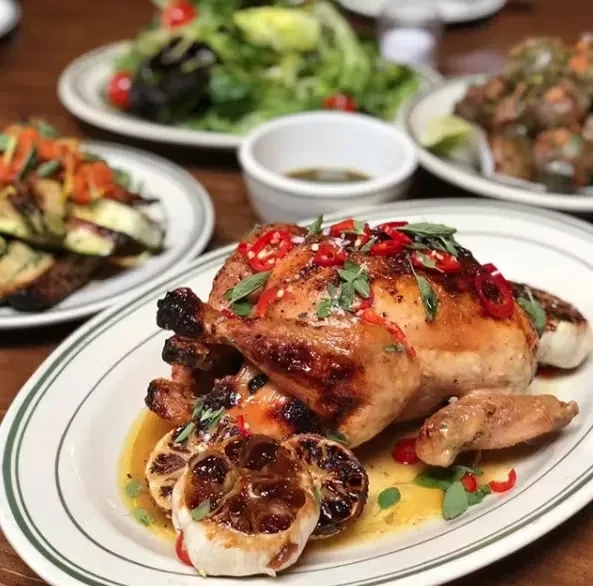 Whole roasted chicken with chili peppers, herbs, and roasted garlic on a plate.