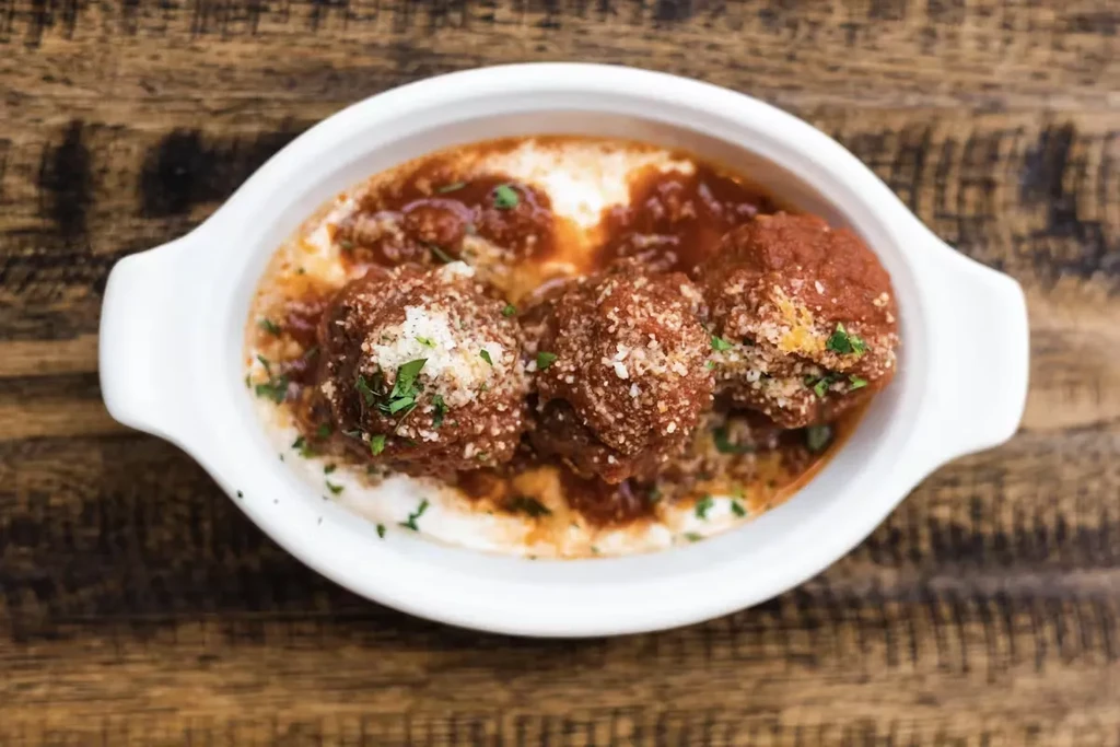 Three large meatballs in sauce with cheese and parsley, in a white dish.