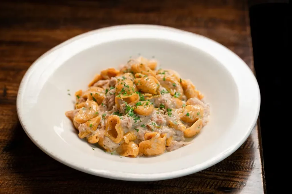 A white bowl of pasta in cream sauce with parsley.