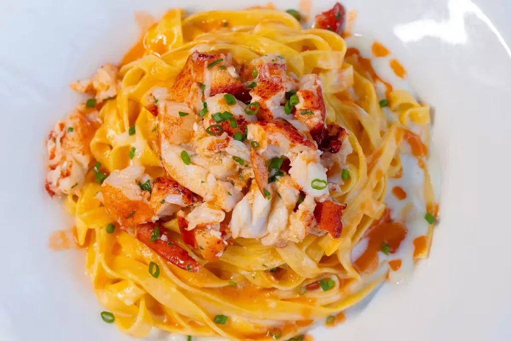 A white plate with tagliatelle pasta, lobster, and sauce.