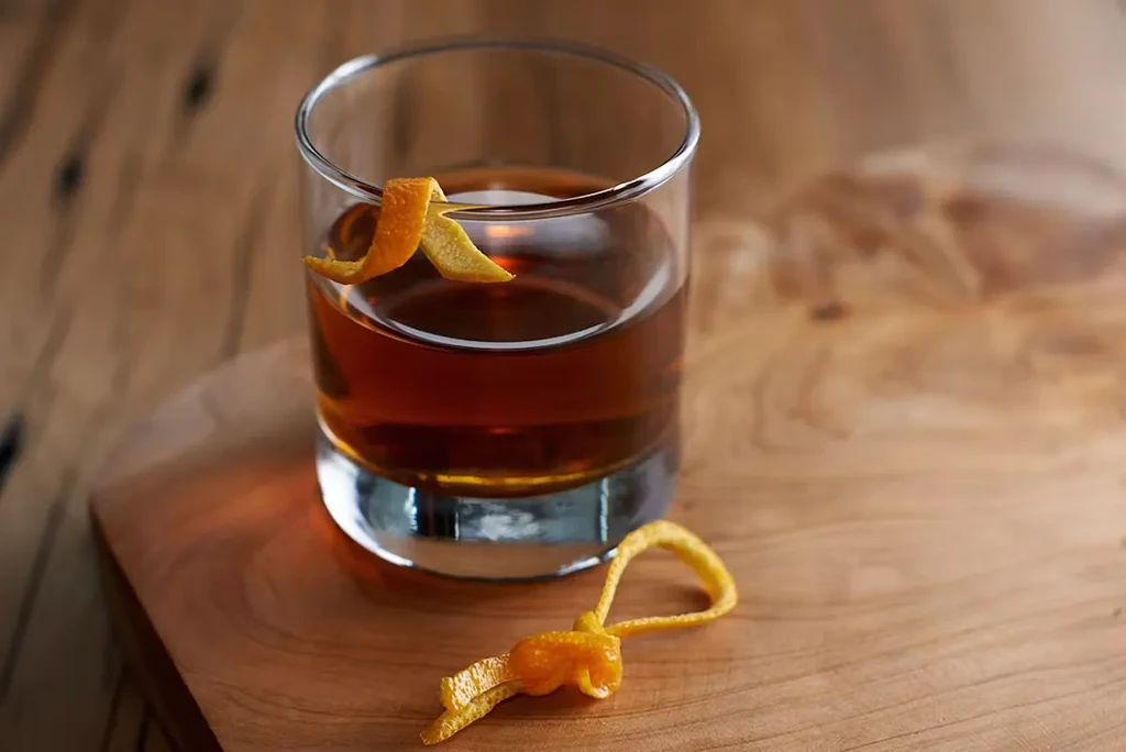 A glass of amber liquor with an orange peel on a wooden surface.