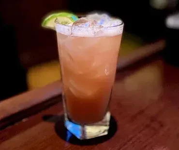 Tall glass with a pink drink, ice, and a lime slice.