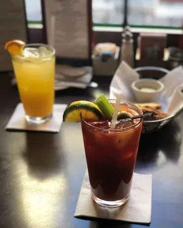 Two cocktails, one orange and one red, on a dark table.