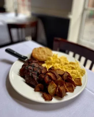 Breakfast plate with steak, scrambled eggs, fried potatoes, and a biscuit.