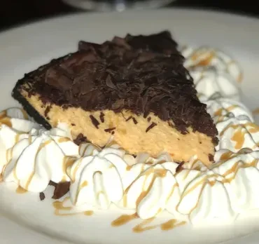 A slice of peanut butter pie, topped with chocolate shavings and whipped cream.