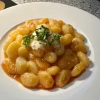 A white plate of gnocchi with tomato sauce and a dollop of cream.