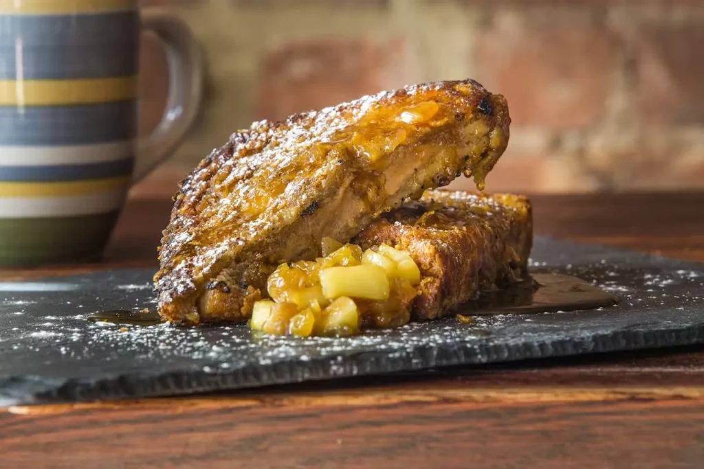 Two pieces of french toast with apple topping and powdered sugar.