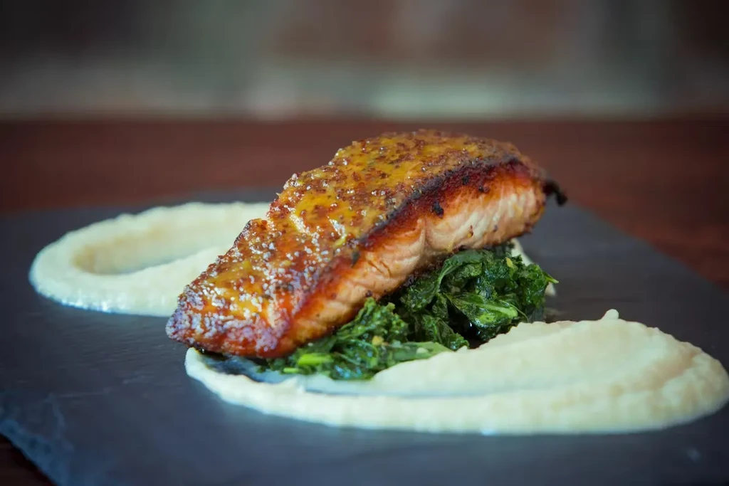 A salmon fillet with mustard glaze on spinach and mashed potatoes.