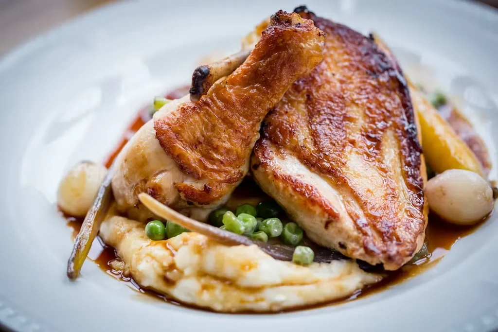 Roasted chicken with gravy, mashed potatoes, peas, and pearl onions on a plate.