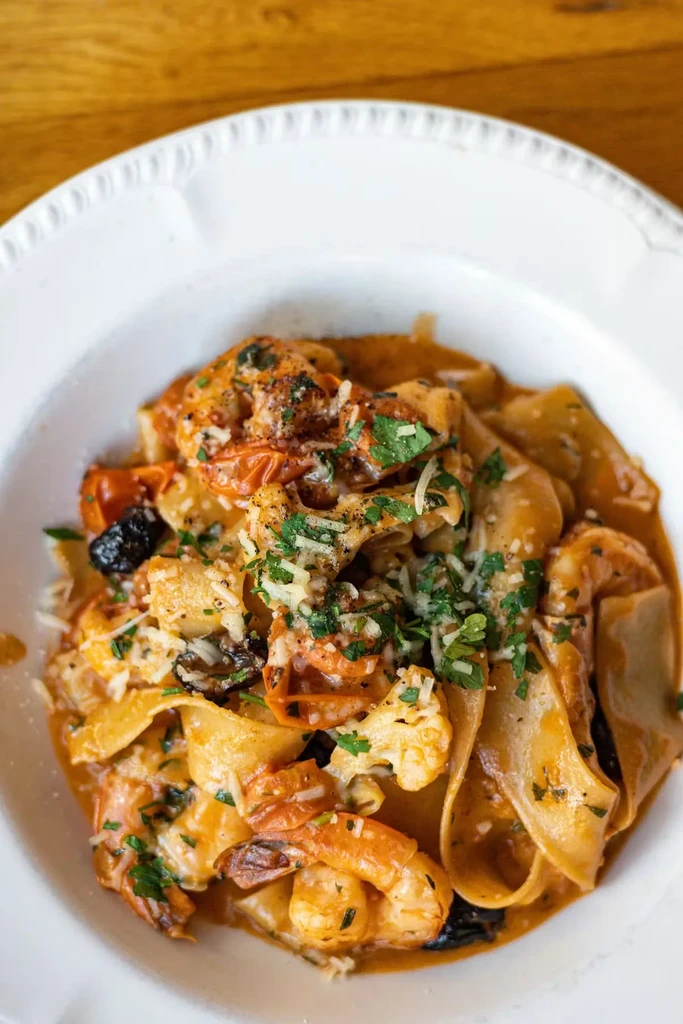 Close-up of a bowl of pasta with shrimp, tomatoes, and parsley.