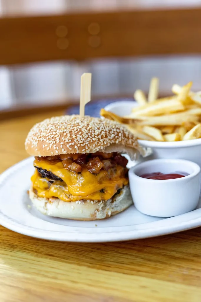 A double cheeseburger with bacon jam, fries, and ketchup on a white plate.