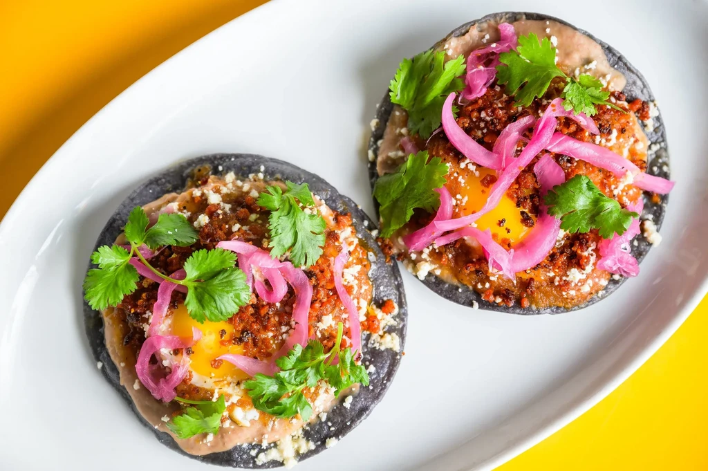 Two huevos rancheros with cilantro and pickled red onions on a white plate.