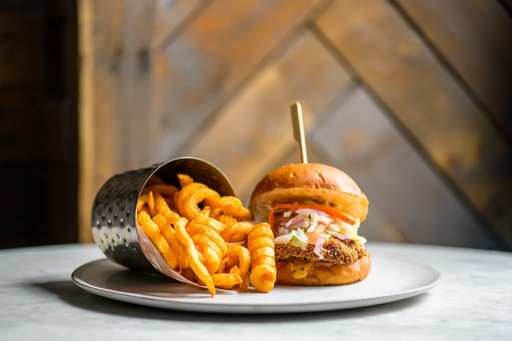 A hamburger and curly fries spilling from a metal cup on a plate.