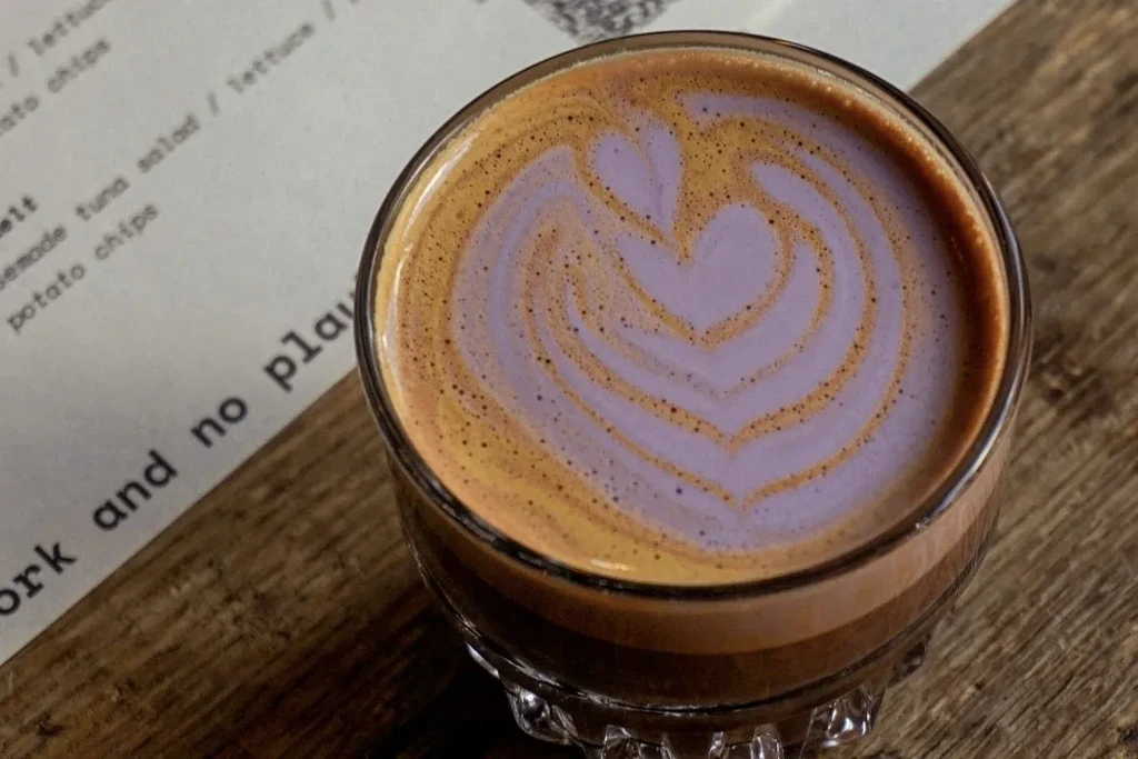Latte art in a glass, next to a menu on a wooden table.