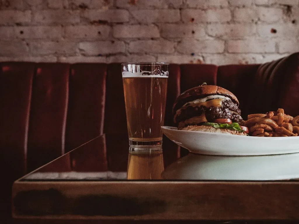 A beer, burger, and fries on a glass table in a bar.
