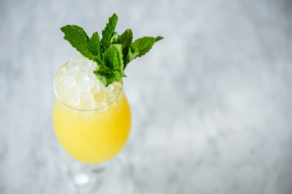 A tall yellow drink with crushed ice and a mint garnish.