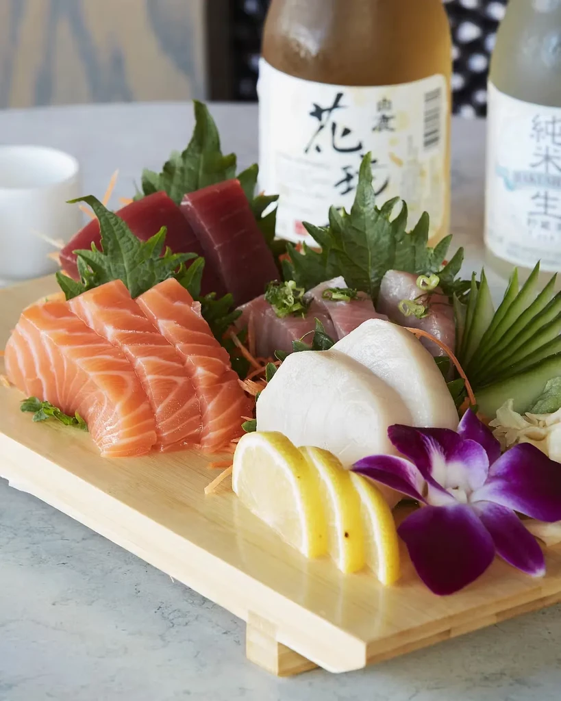 Sashimi platter with tuna, salmon, and white fish, with sake bottles behind.