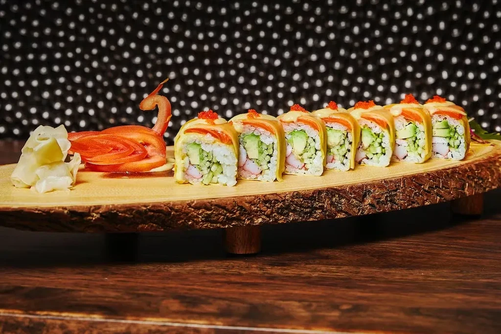 Sushi rolls, a tomato swan, and ginger on a rustic wooden board.