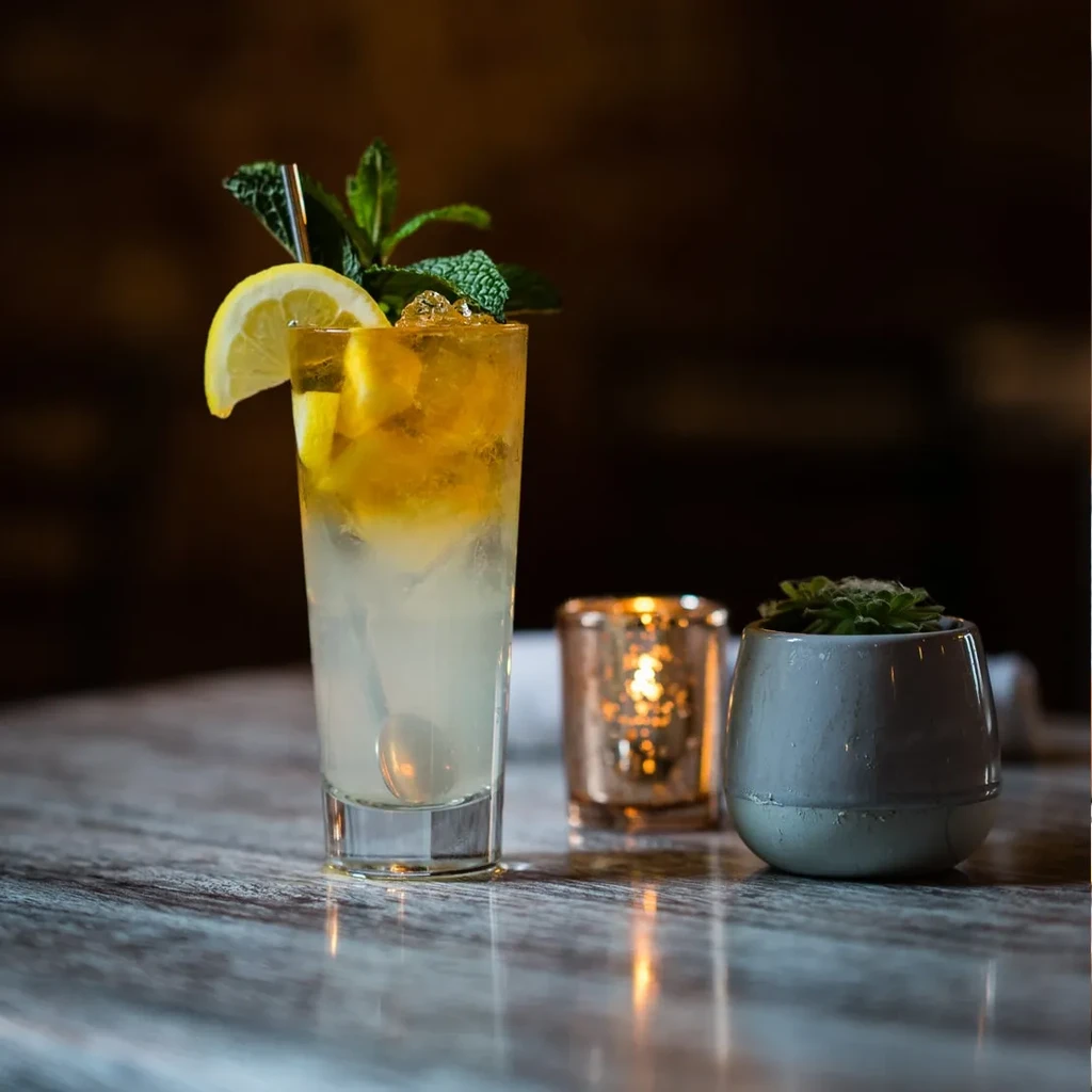 Tall drink with lemon, mint, and ice, beside a candle and plant.