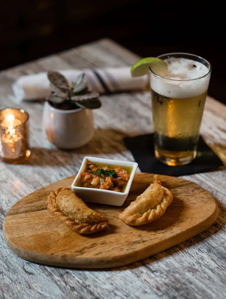 Two empanadas, salsa, and a beer with a lime on a wooden board.