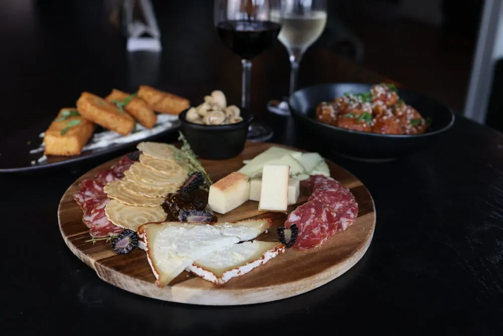 A charcuterie board with cheese, salami, and crackers, plus other dishes and wine.