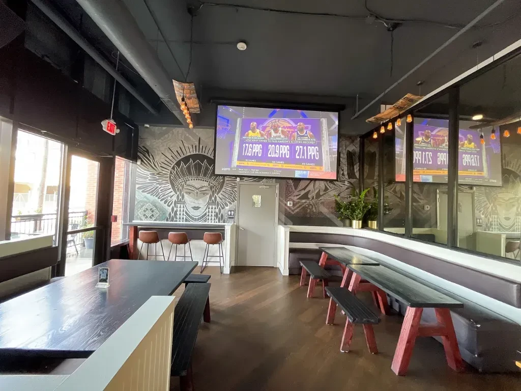 Modern bar or restaurant interior with TV screens and long tables.