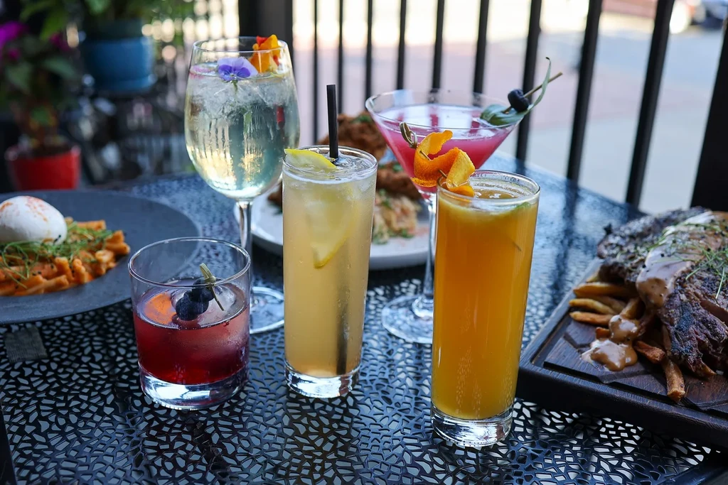 Assortment of cocktails and food on a black patio table.