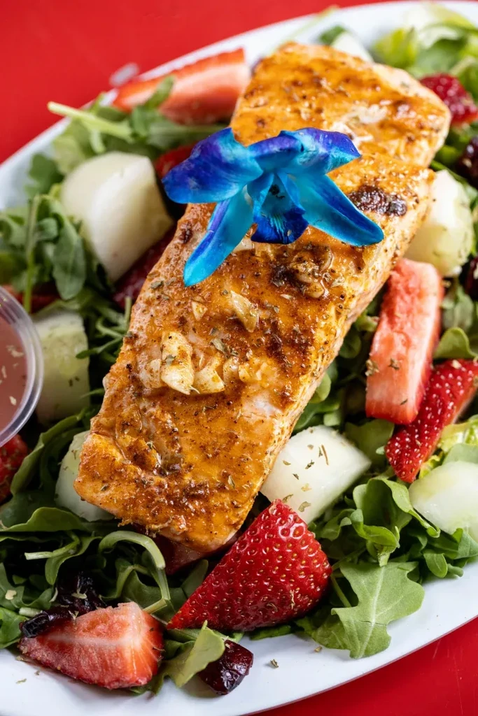 Grilled salmon fillet with arugula, strawberries, melon, and blue orchid garnish.