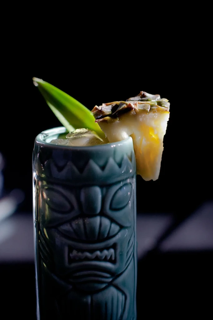 A blue tiki mug with a drink, pineapple slice, and green leaf.