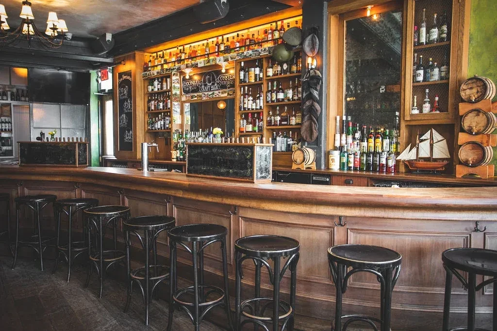 A long, elegant wooden bar with numerous barstools and bottles of alcohol.