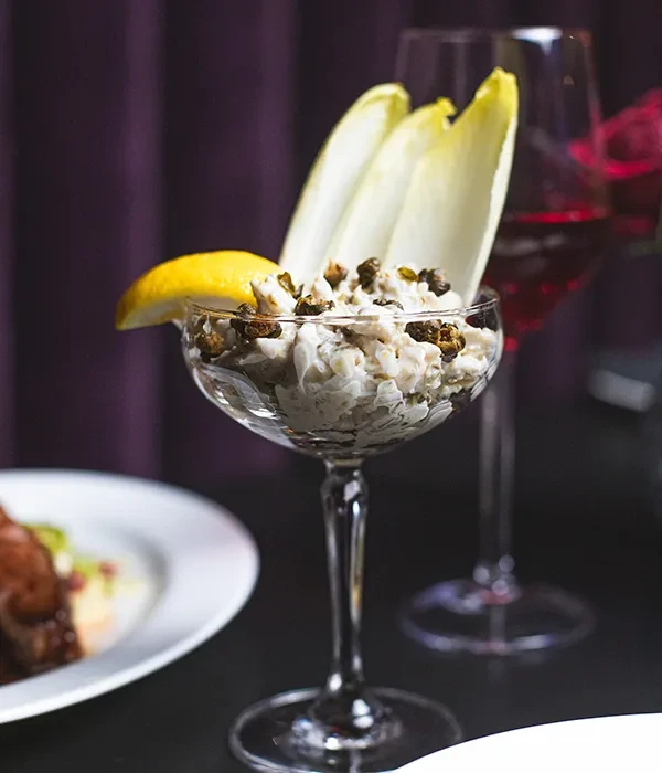 Crab salad with endive and lemon slice in a coupe glass.