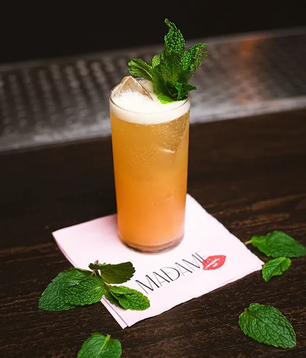 A tall, amber cocktail with foam, ice, and mint garnish.