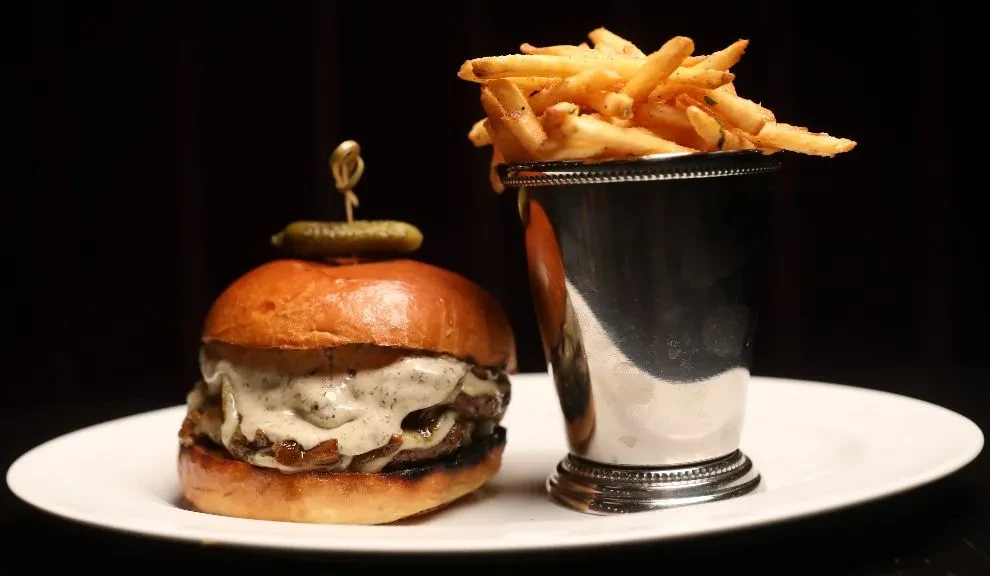 A gourmet burger with fries in a silver cup on a white plate.