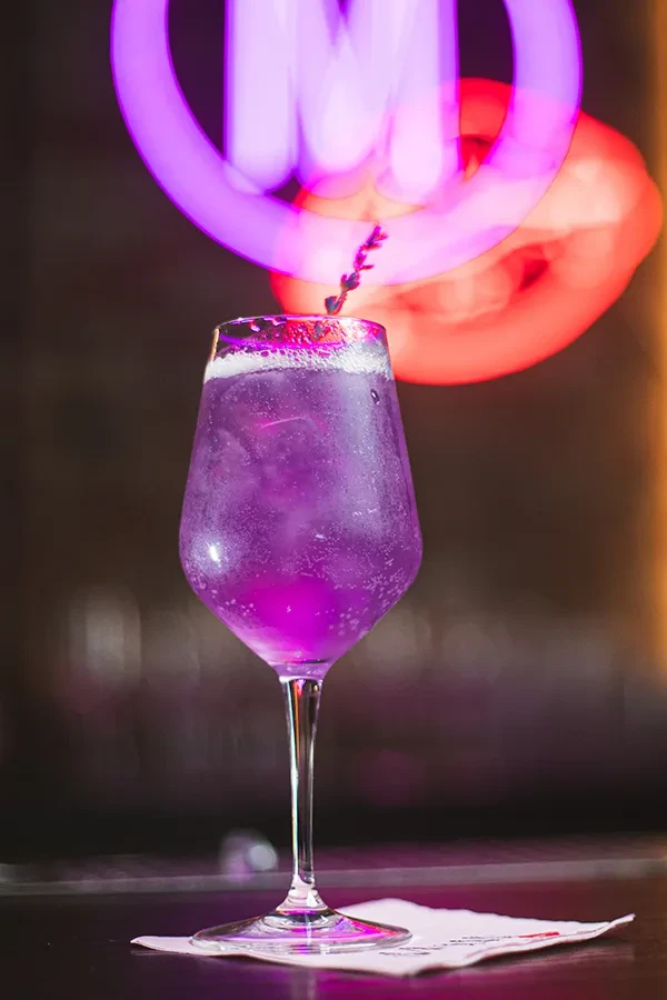 A purple cocktail with a lavender sprig on a bar counter.