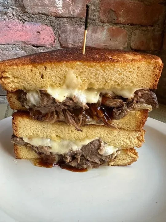 A thick-cut beef and cheese sandwich on a white plate.