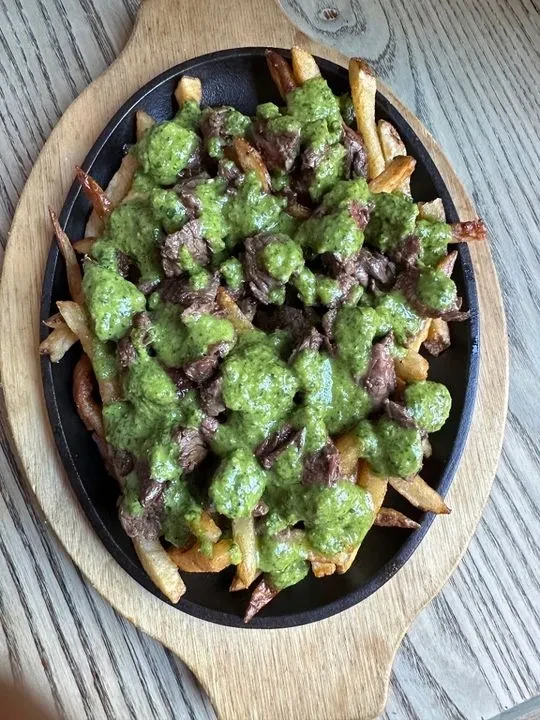 Fries topped with meat and a green sauce in a black skillet.