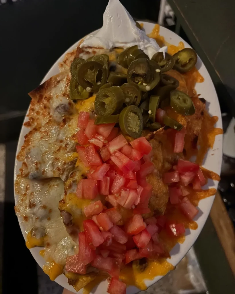 Plate of nachos topped with tomatoes, jalapeños, cheese, and sour cream.