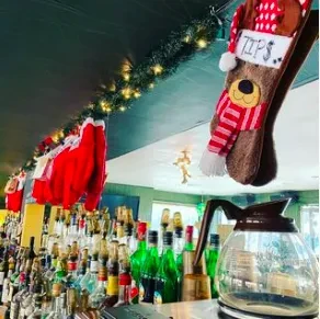 Bar decorated with holiday garland and stockings above liquor bottles.