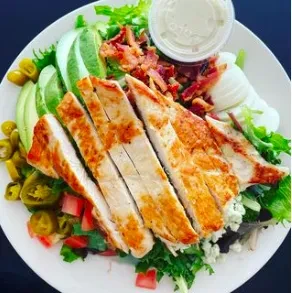 A chicken cobb salad with avocado, bacon, and dressing on a white plate.