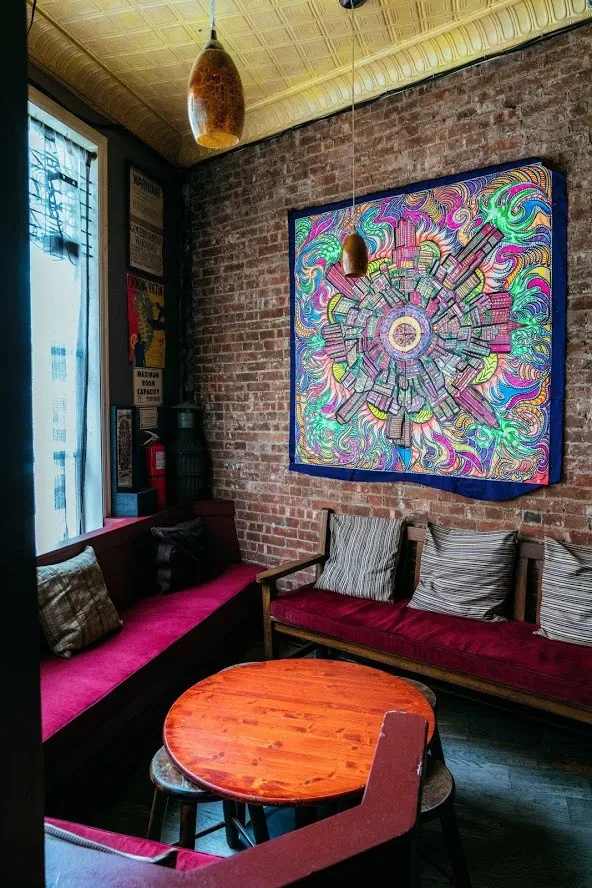 A colorful tapestry, red benches, and a wooden table in a rustic room.