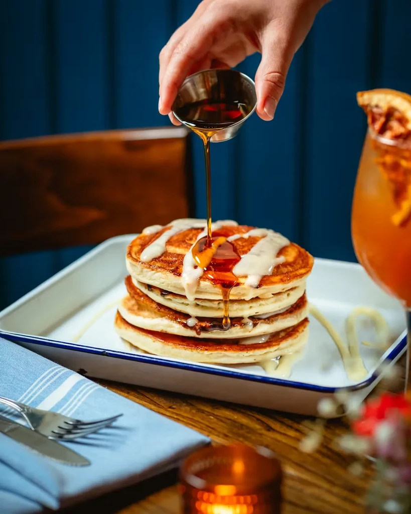 Maple syrup is poured over a stack of pancakes with white icing.