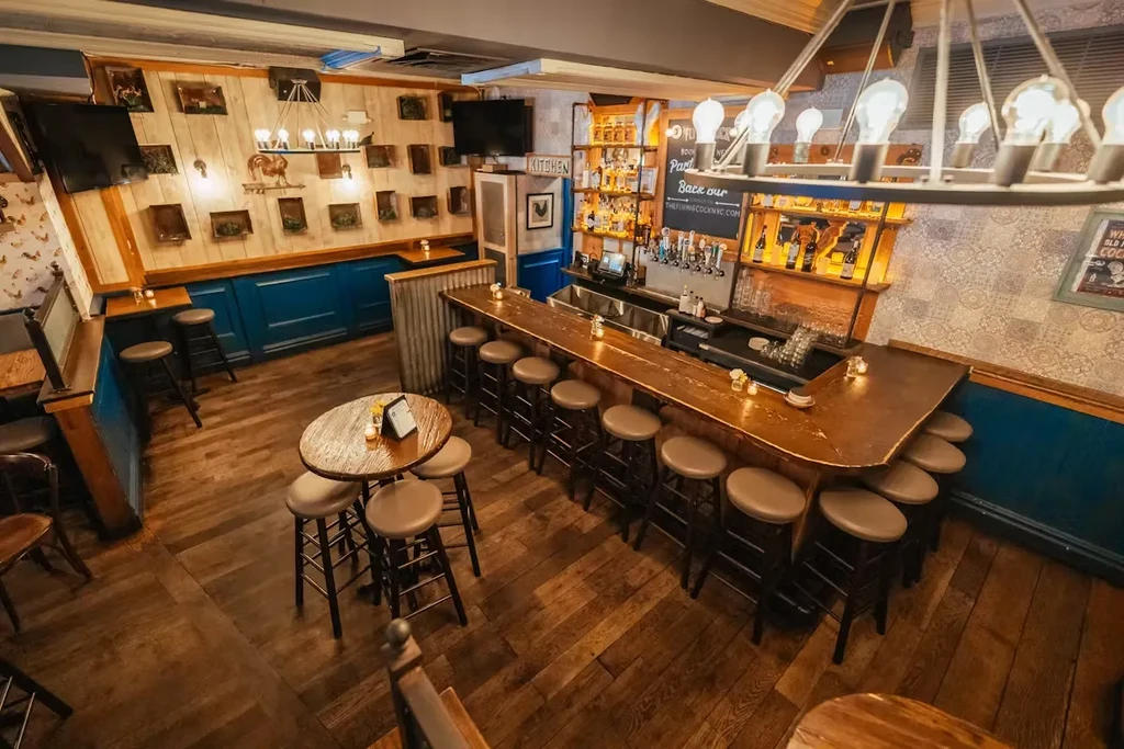 A rustic-style bar with wooden floors, a long bar, and small tables.