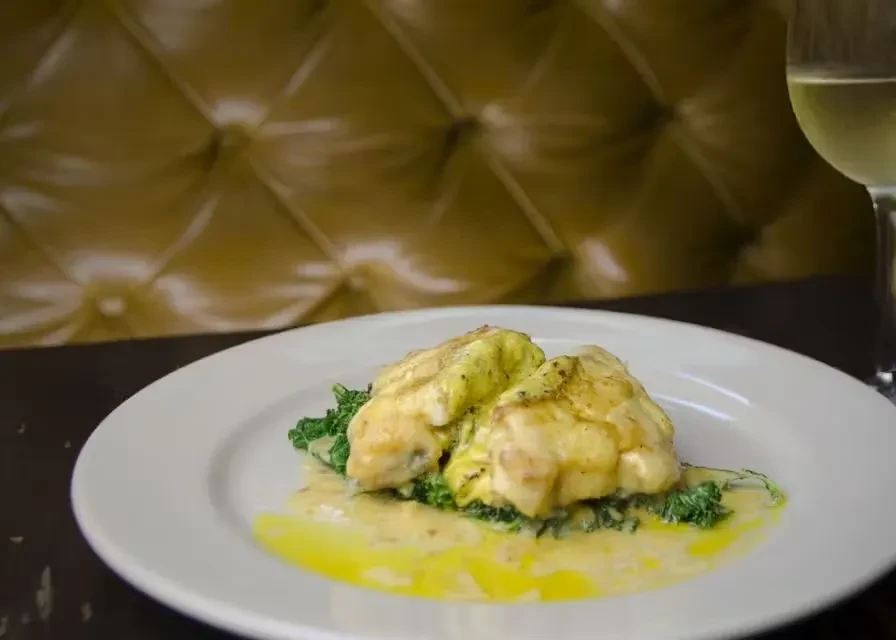 Creamy chicken dish on greens, white plate, wine glass.