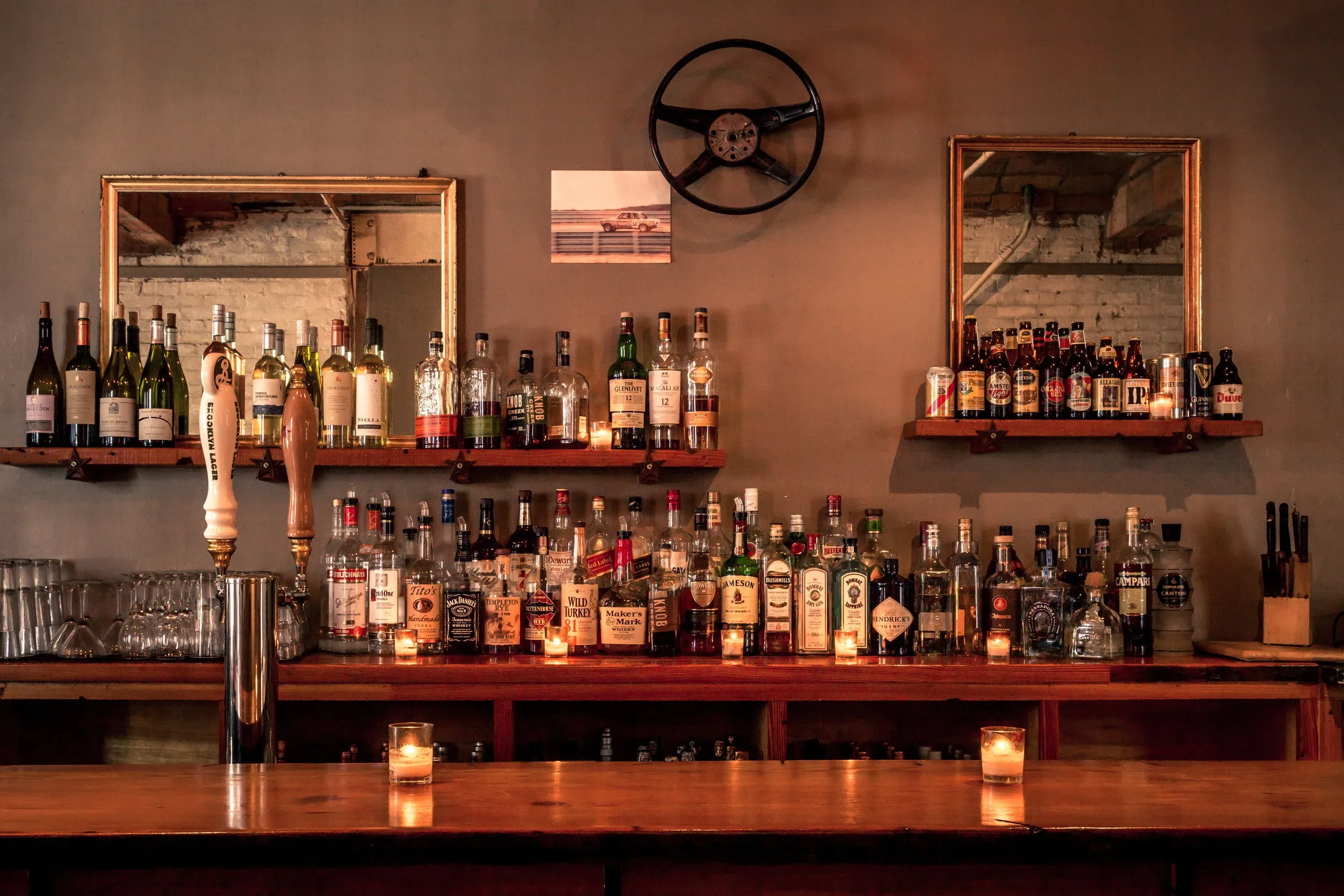 A dimly lit bar with numerous bottles of alcohol and two mirrors.