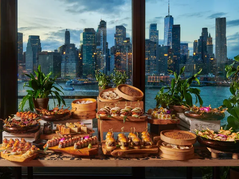 Food buffet overlooking the illuminated New York City skyline at dusk.