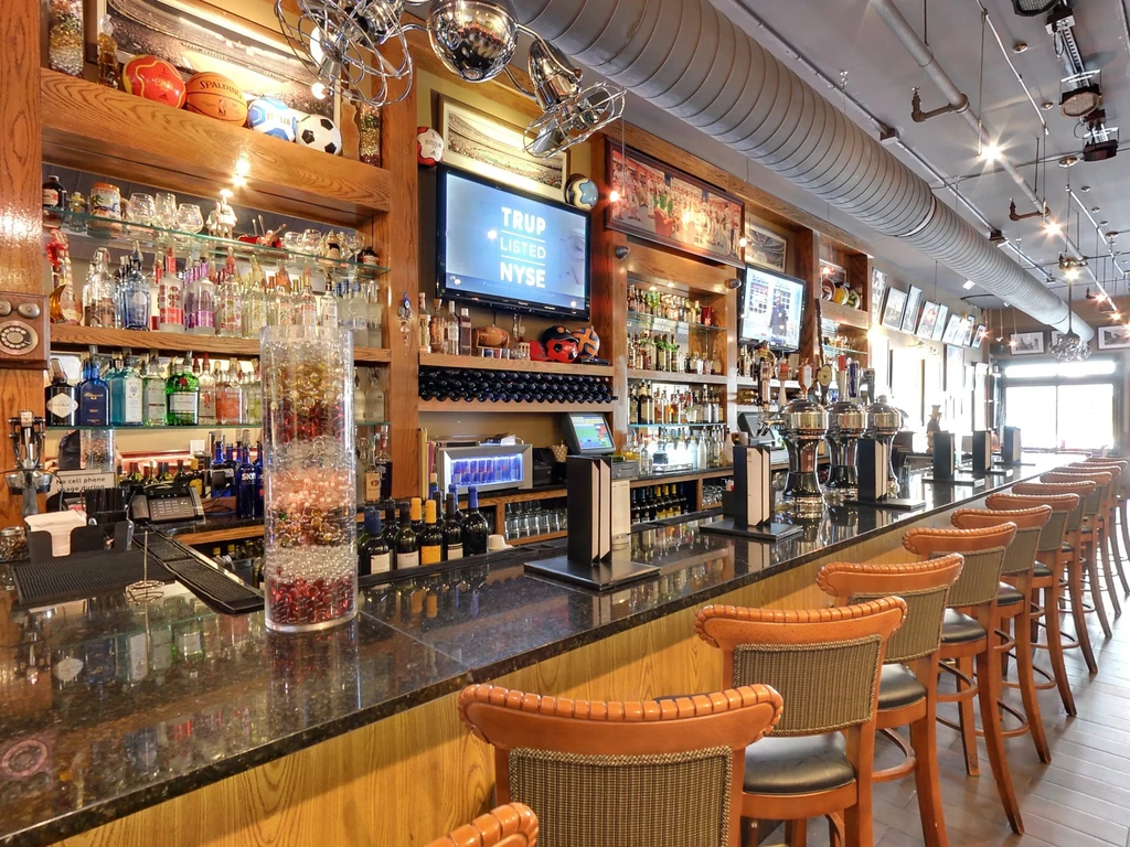 Empty sports bar with dark granite counter, liquor shelves, and multiple TVs.